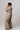 Person wearing a beige trench coat and pants on a plain background