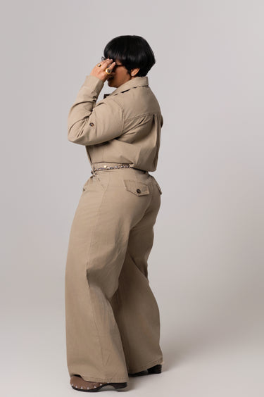 Person wearing a beige trench coat and pants on a plain background